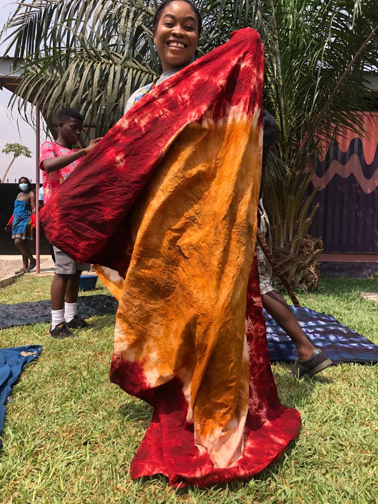 A visitor holding up her red and orange tie-dye cloth