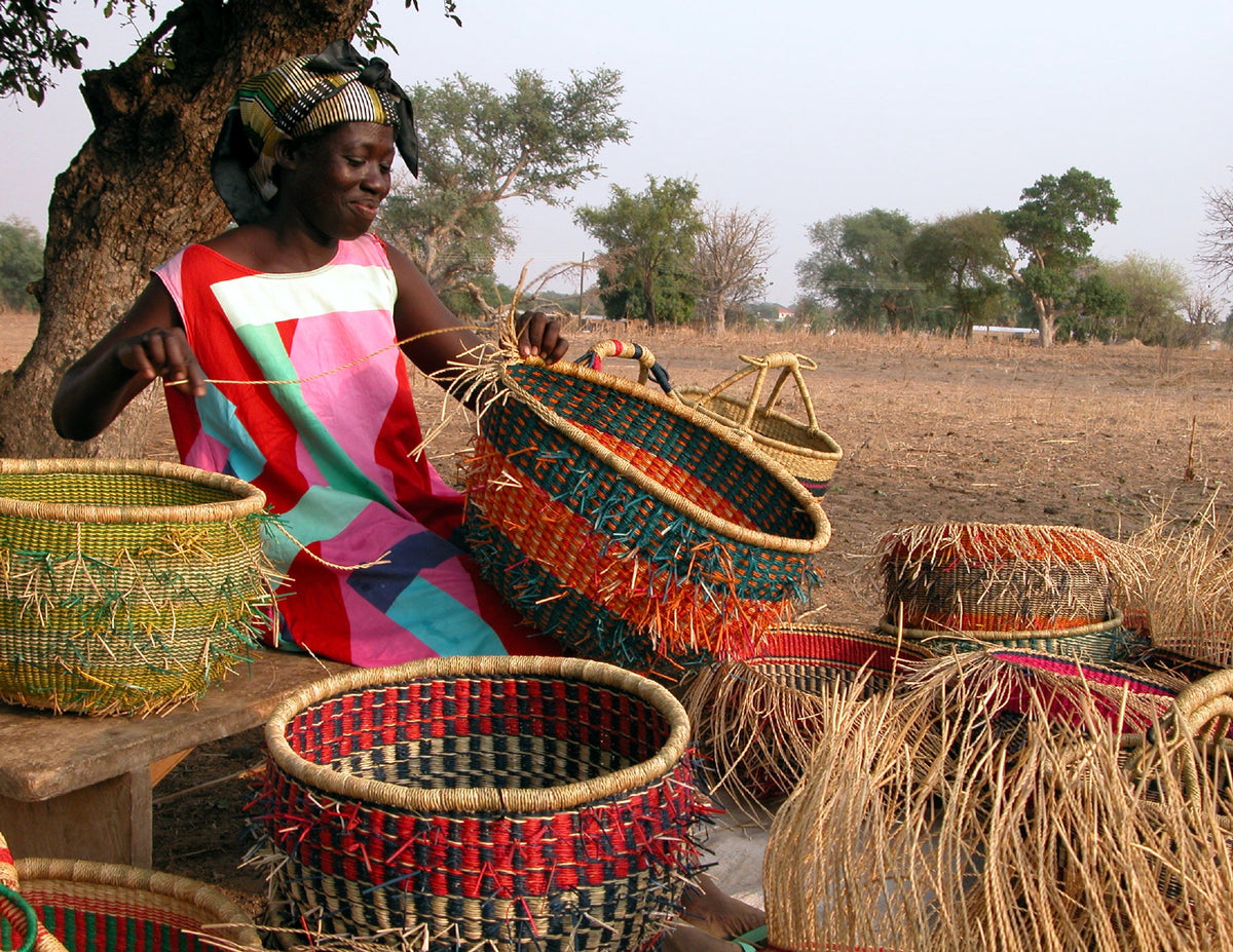 Artisan weaving a colorful basket outdoors, surrounded by finished baskets