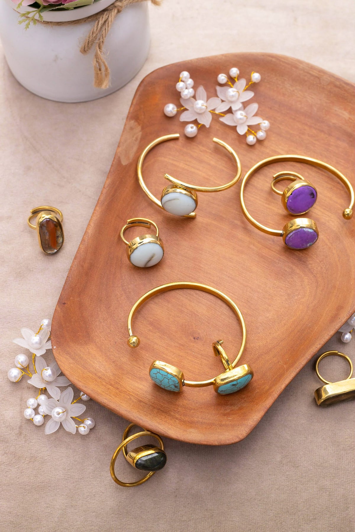 Brass cuff bracelets and rings set with colored stones on a wooden tray