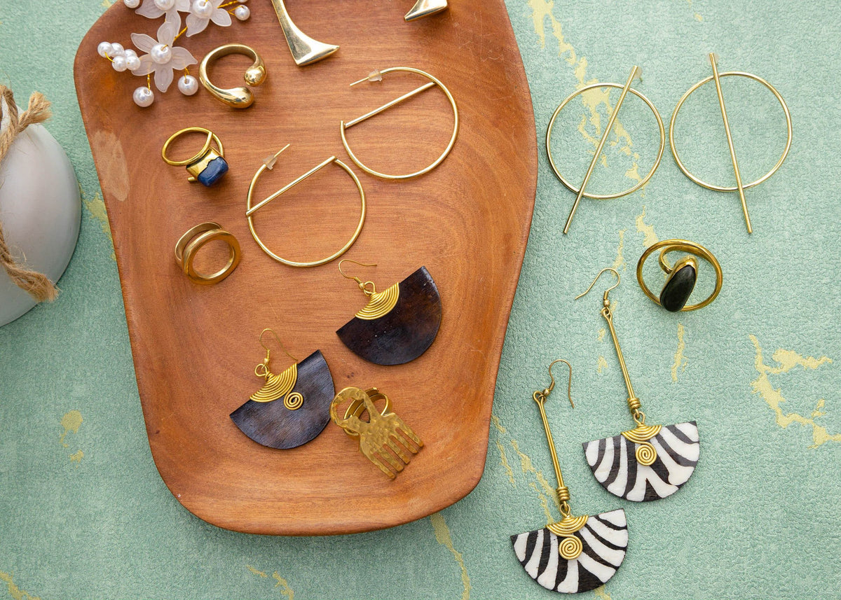 Handcrafted brass earrings and rings arranged on a wooden tray